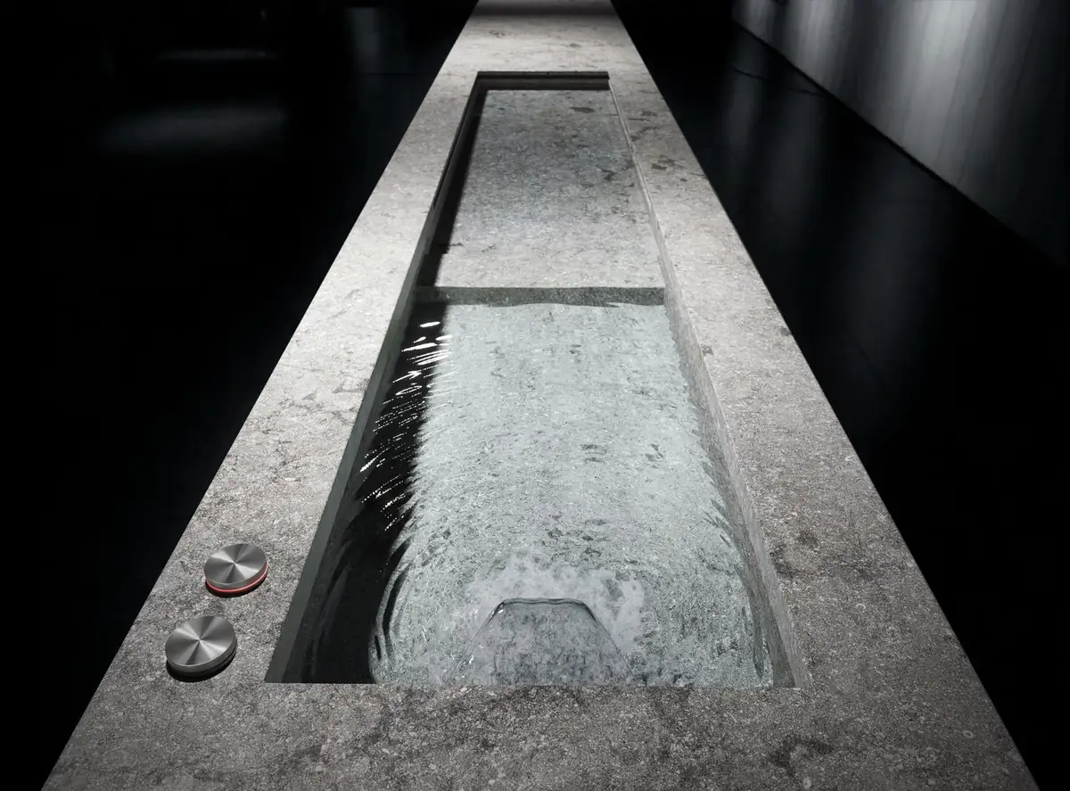 Pieza alargada de piedra gris llena de agua con dos mandos metálicos en el borde