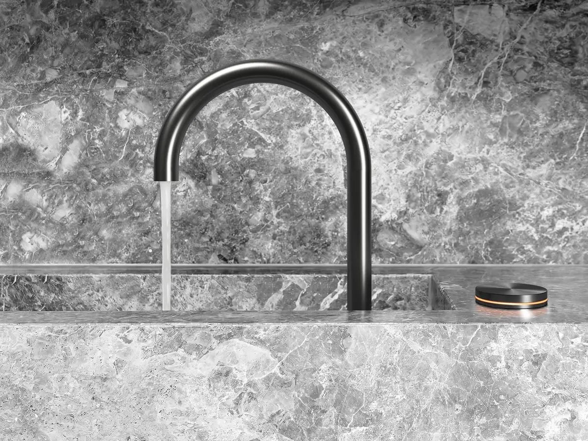 Grifo de cocina oscuro de caño curvo sobre fregadero de mármol gris, con un mando circular al lado