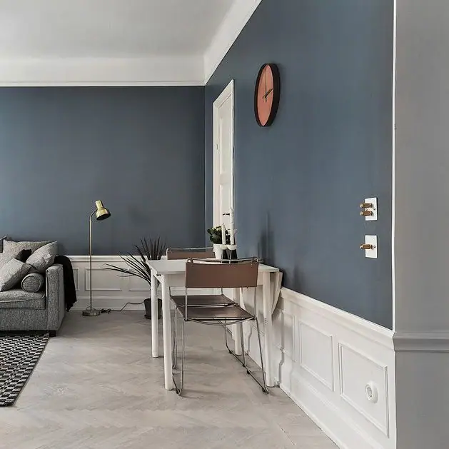 Salón con pared azul, zócalo blanco con molduras y mecanismos de placa blanca con mandos de latón