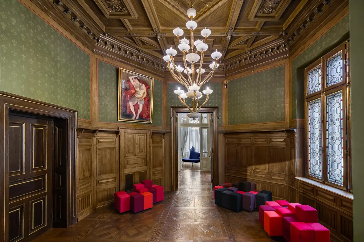 Sala histórica con artesonado, araña de cristal, paredes enteladas y pavimento de madera oscura.
