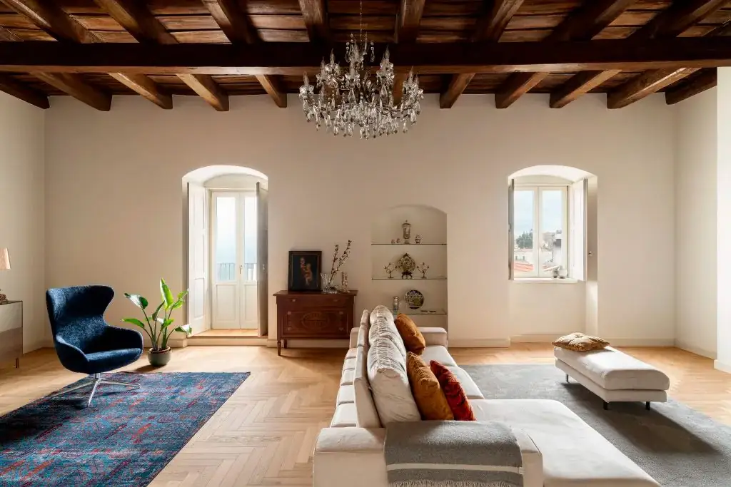 Salón con techo de vigas de madera, lámpara de araña y pavimento de roble claro en espiga.