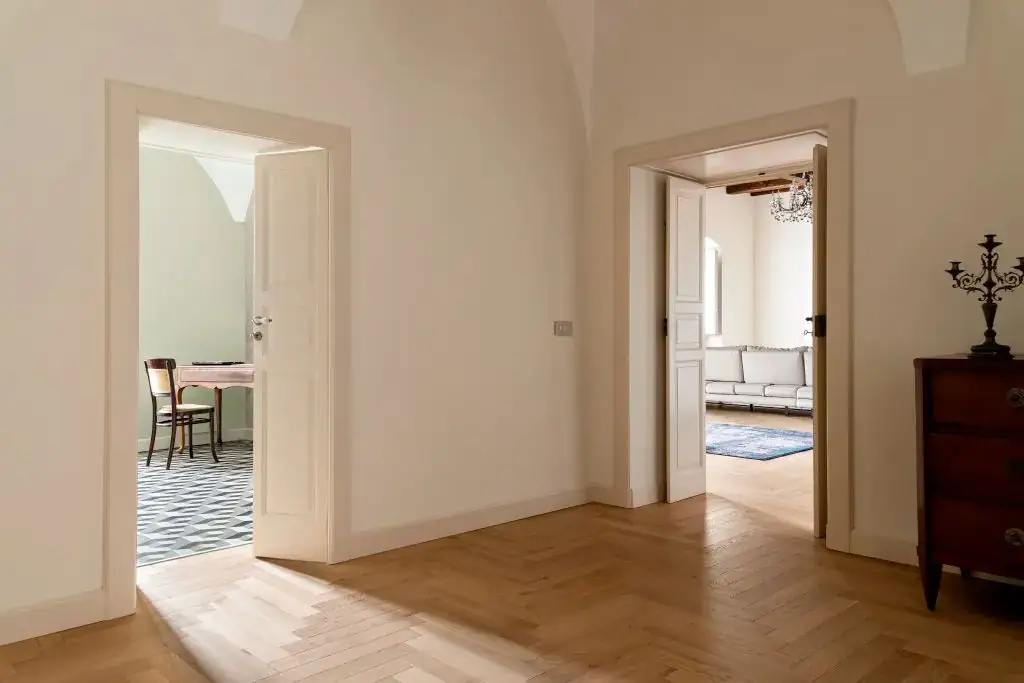 Distribuidor con dos puertas abiertas y pavimento de roble en espiga que continúa en el salón.