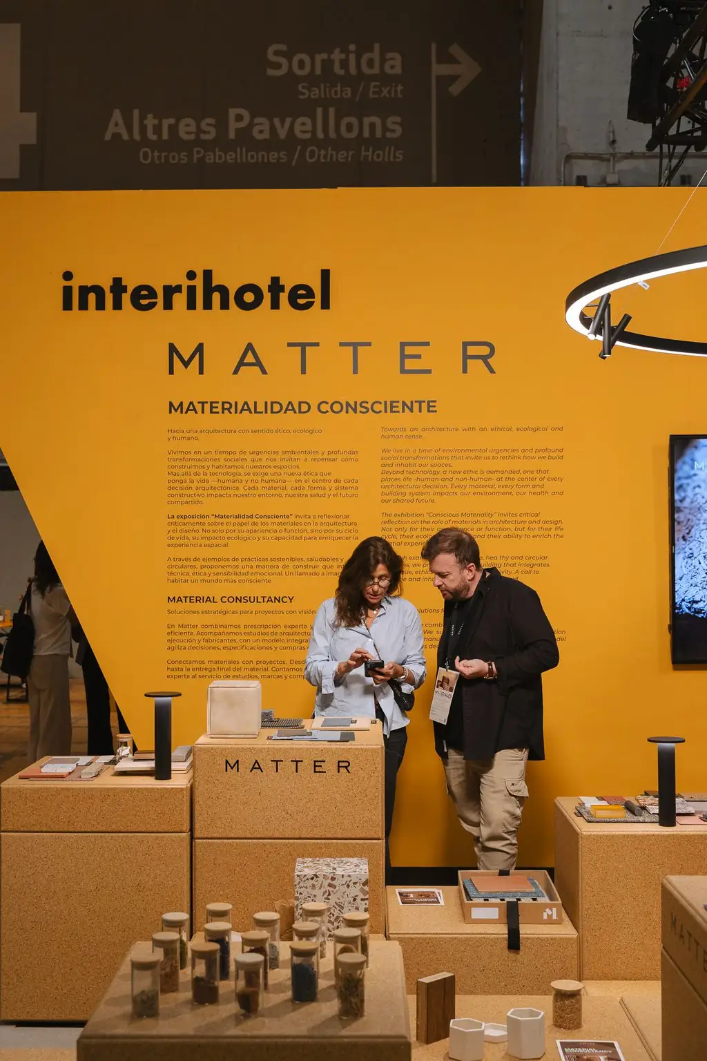 Dos visitantes consultan muestras ante el panel Materialidad Consciente