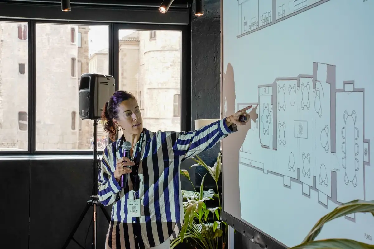 Ponente señalando una planta proyectada en la pantalla de la sala de conferencias.