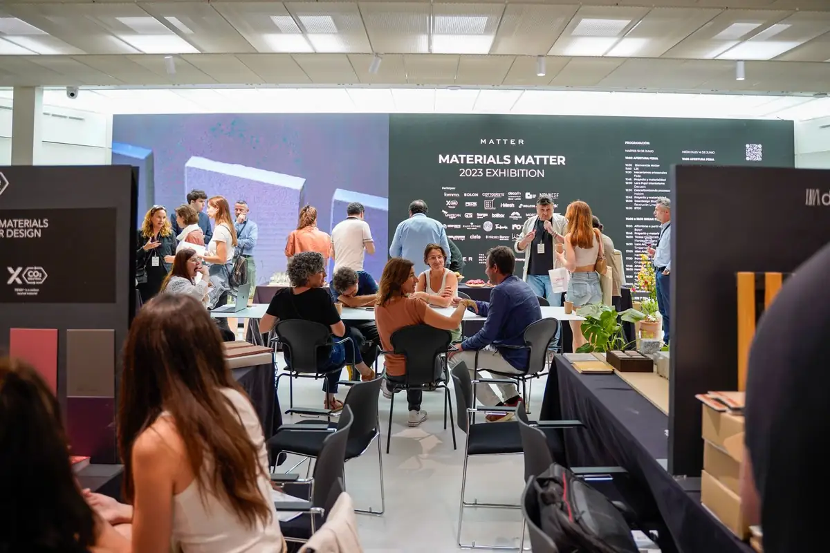 Zona de descanso con mesas y sillas ante el panel de Materials Matter 2023 Exhibition con las marcas y el programa.