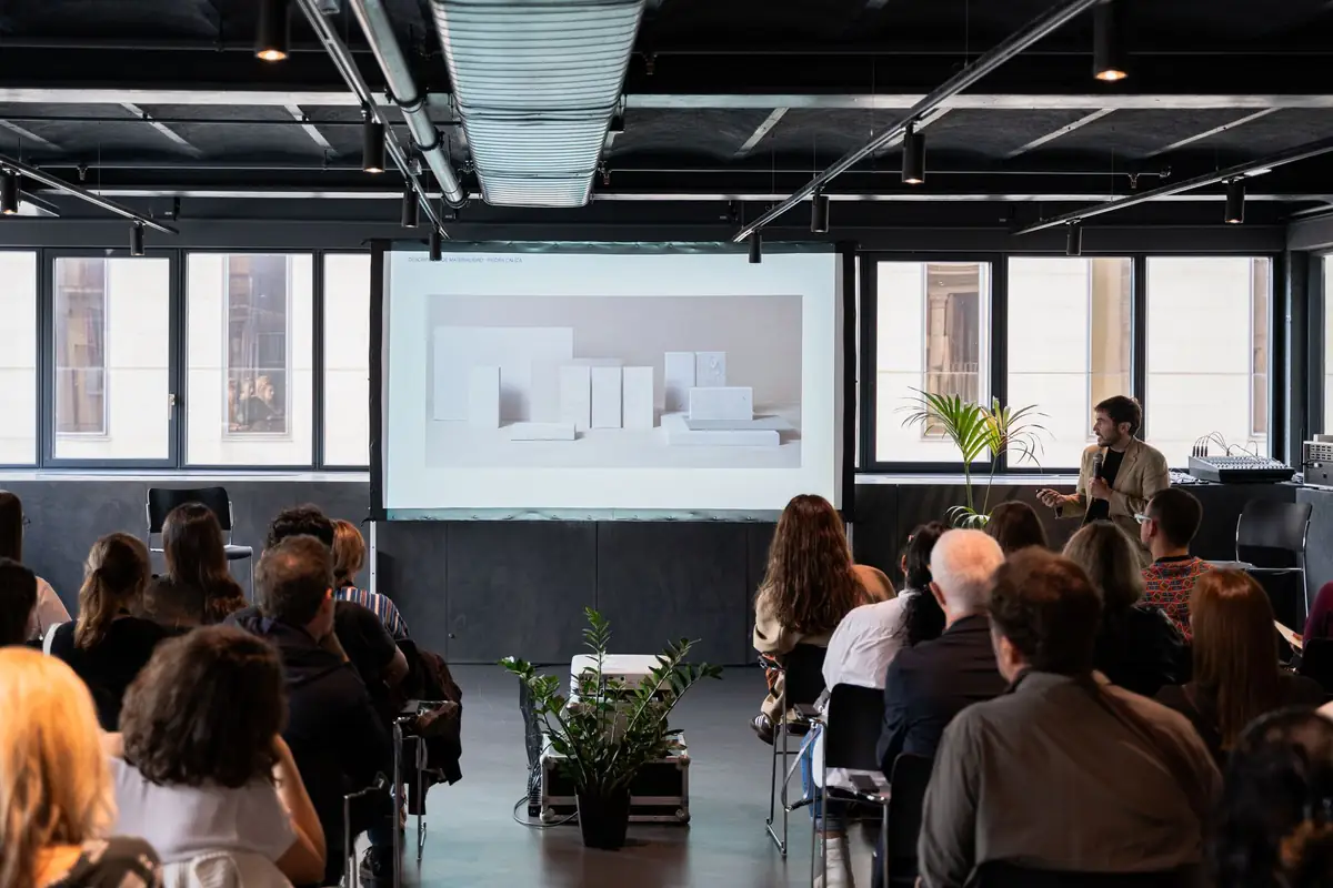 Público asistiendo a una ponencia en la planta superior del COAC, con una maqueta blanca proyectada en pantalla.