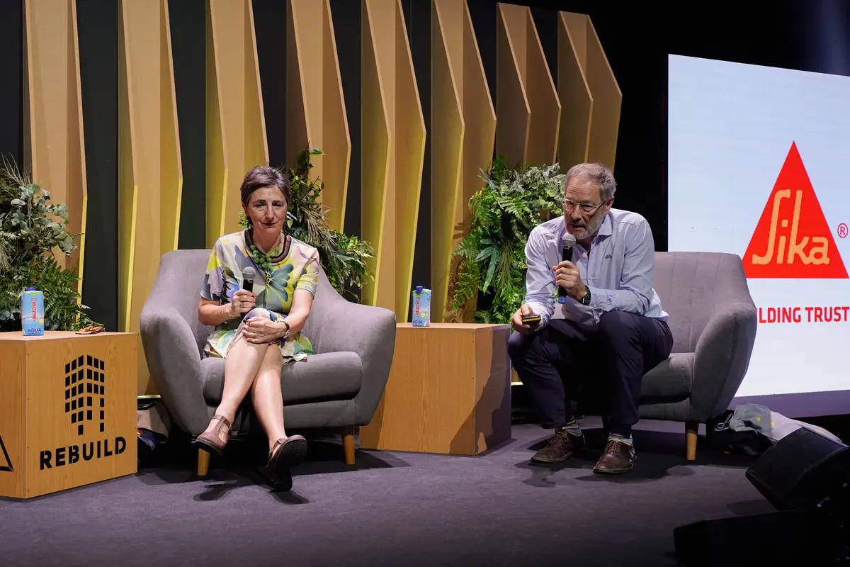 Una ponente y un ponente conversan sentados en butacas en el escenario, junto al logotipo de Sika