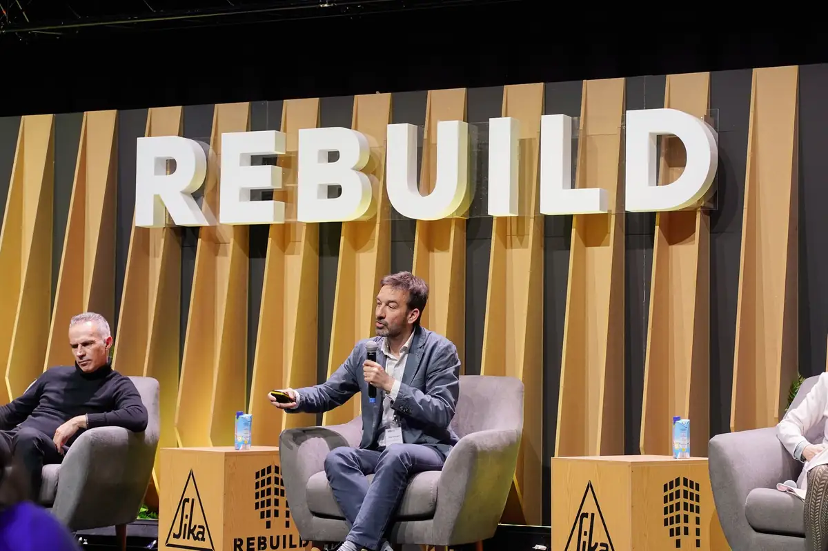 Un ponente presenta un proyecto desde su butaca en el escenario de REBUILD