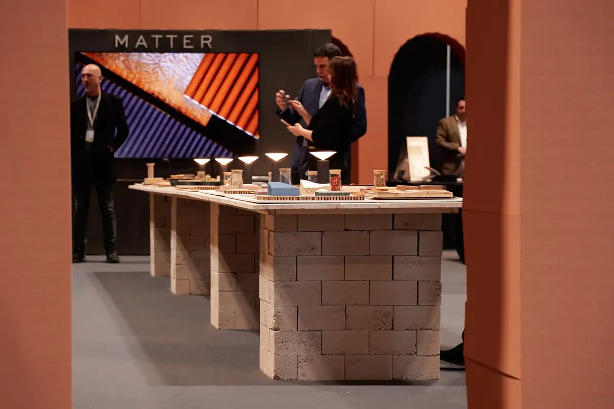 Mesa larga de muestras de materiales sobre bases de bloques, con la pantalla de Matter al fondo