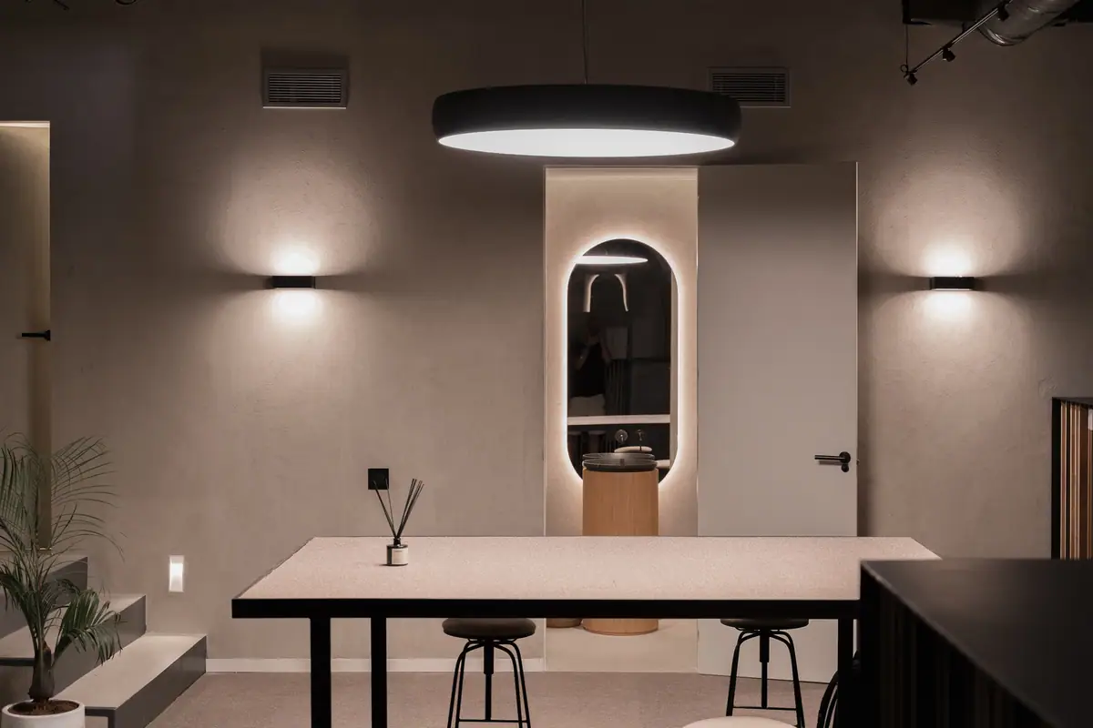 Mesa alta y lavabo con espejo ovalado retroiluminado en un espacio de tonos grises