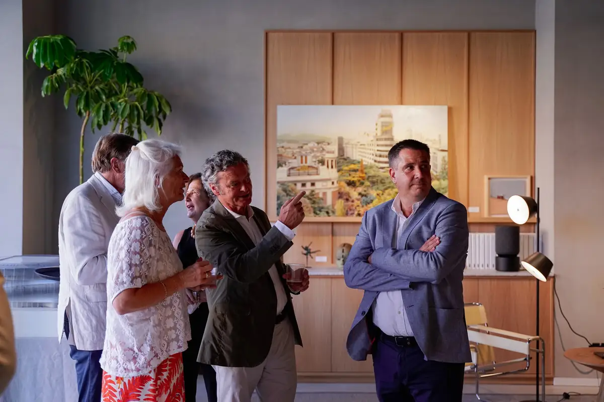 Invitados conversan delante de un cuadro con una vista urbana