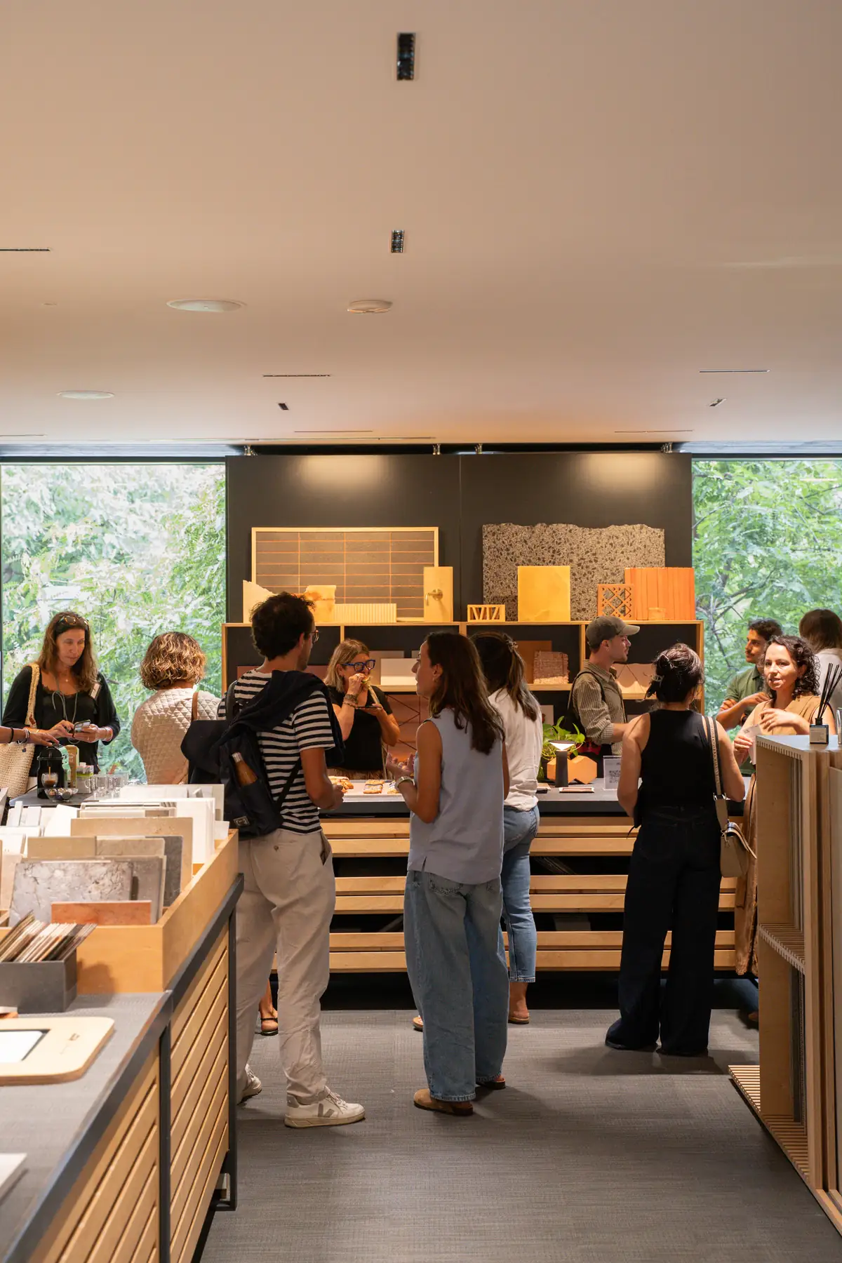 Asistentes conversando de pie en la Materioteca de Matter Barcelona, con muestras de materiales al fondo y ventanales a la vegetación.
