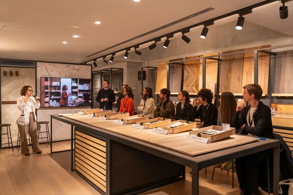 Una ponente con micrófono se dirige a los arquitectos sentados alrededor de la mesa de muestras de Matter Madrid