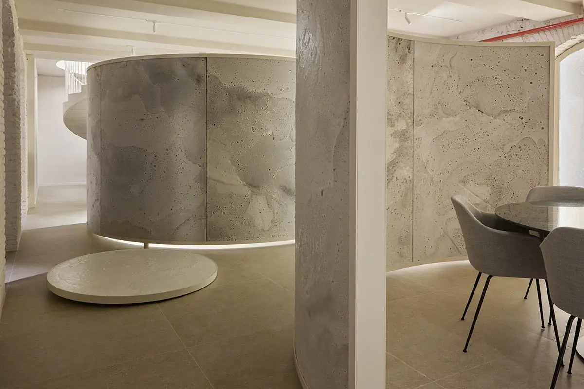 Volumen cilíndrico de material blanco texturizado sobre una base circular, junto a un pilar
