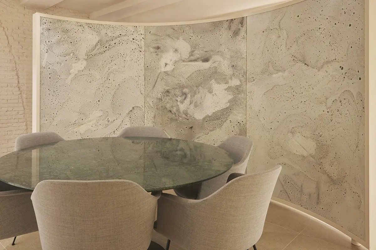 Sala de reuniones con mesa redonda verde y sillas tapizadas, rodeada por un biombo curvo de material blanco texturizado