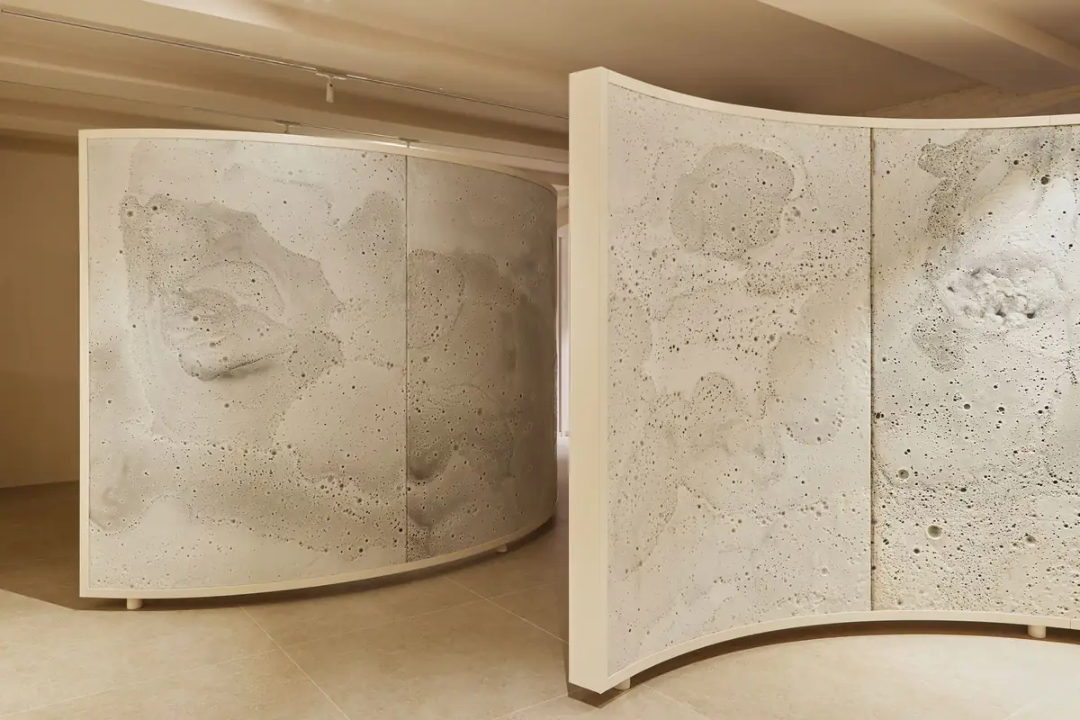 Dos biombos curvos de gran formato con superficie blanca texturizada en una sala de techo bajo