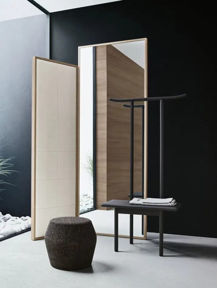Paravento de madera y tela, silla de madera oscura con respaldo alto y puf de corcho negro delante de una pared negra.