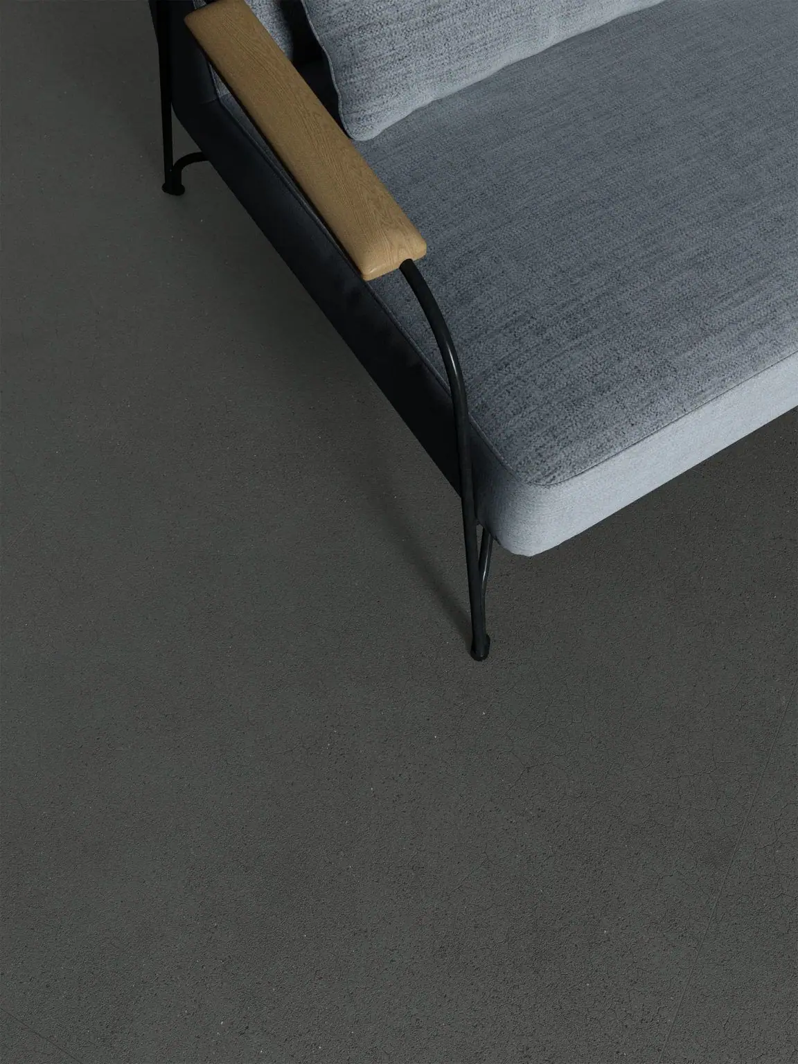 Pavimento gris oscuro de Matter Inva visto desde arriba, con una butaca tapizada en gris claro de estructura metálica negra y brazo de madera.