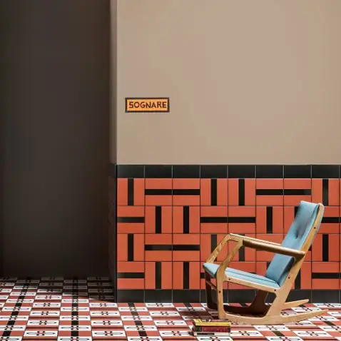 Mecedora de madera con cojín azul ante un zócalo de baldosas naranjas y negras, con pared beige y suelo estampado en rojo y blanco