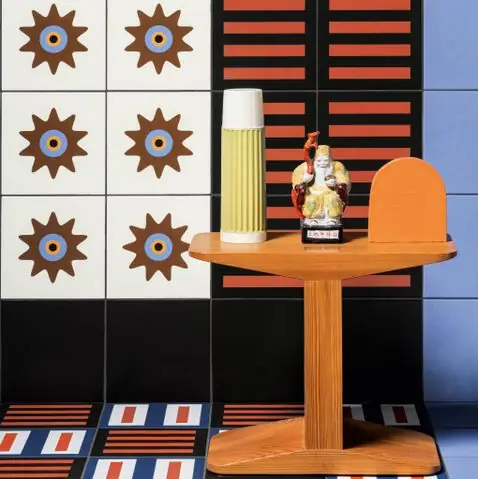Mesa auxiliar de madera ante una pared de baldosas con estrellas marrones, bandas naranjas sobre negro y azul claro, con suelo a rayas