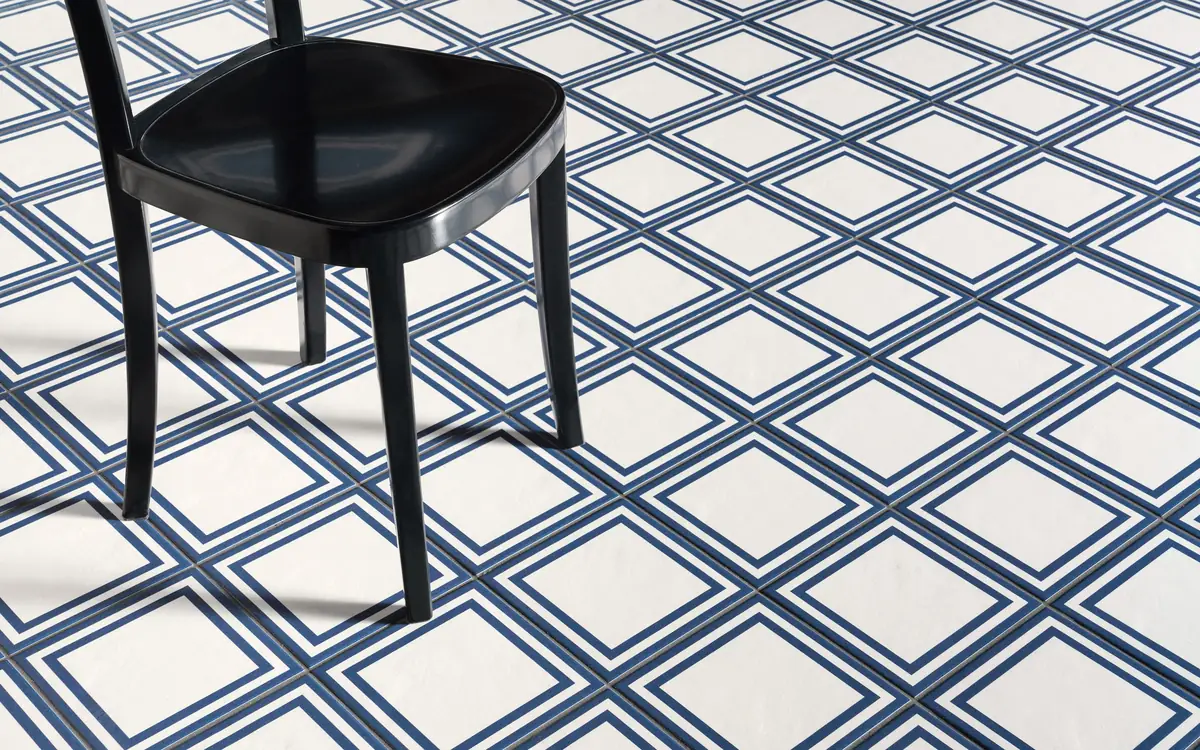 Silla negra sobre un suelo de baldosas blancas con un doble marco azul que forman una retícula de rombos