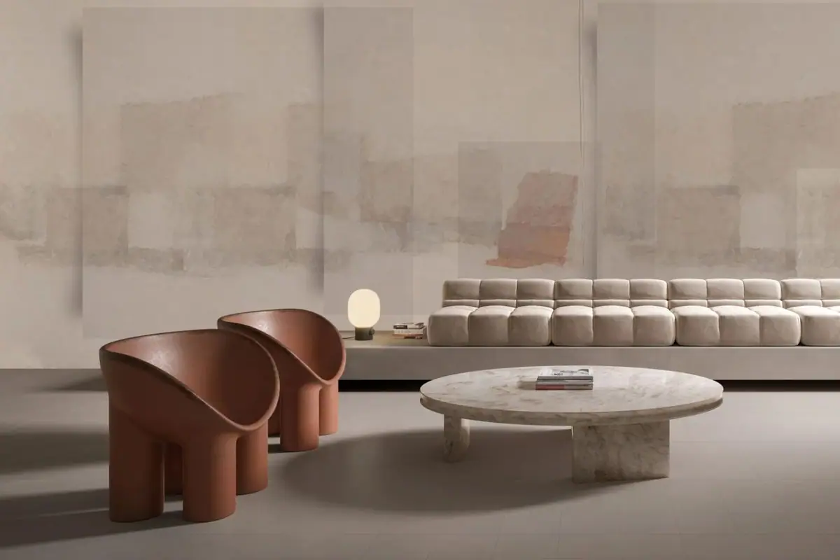 Salón con sofá modular y butacas de cuero rojizo ante una pared con planos abstractos en tonos crema y arena