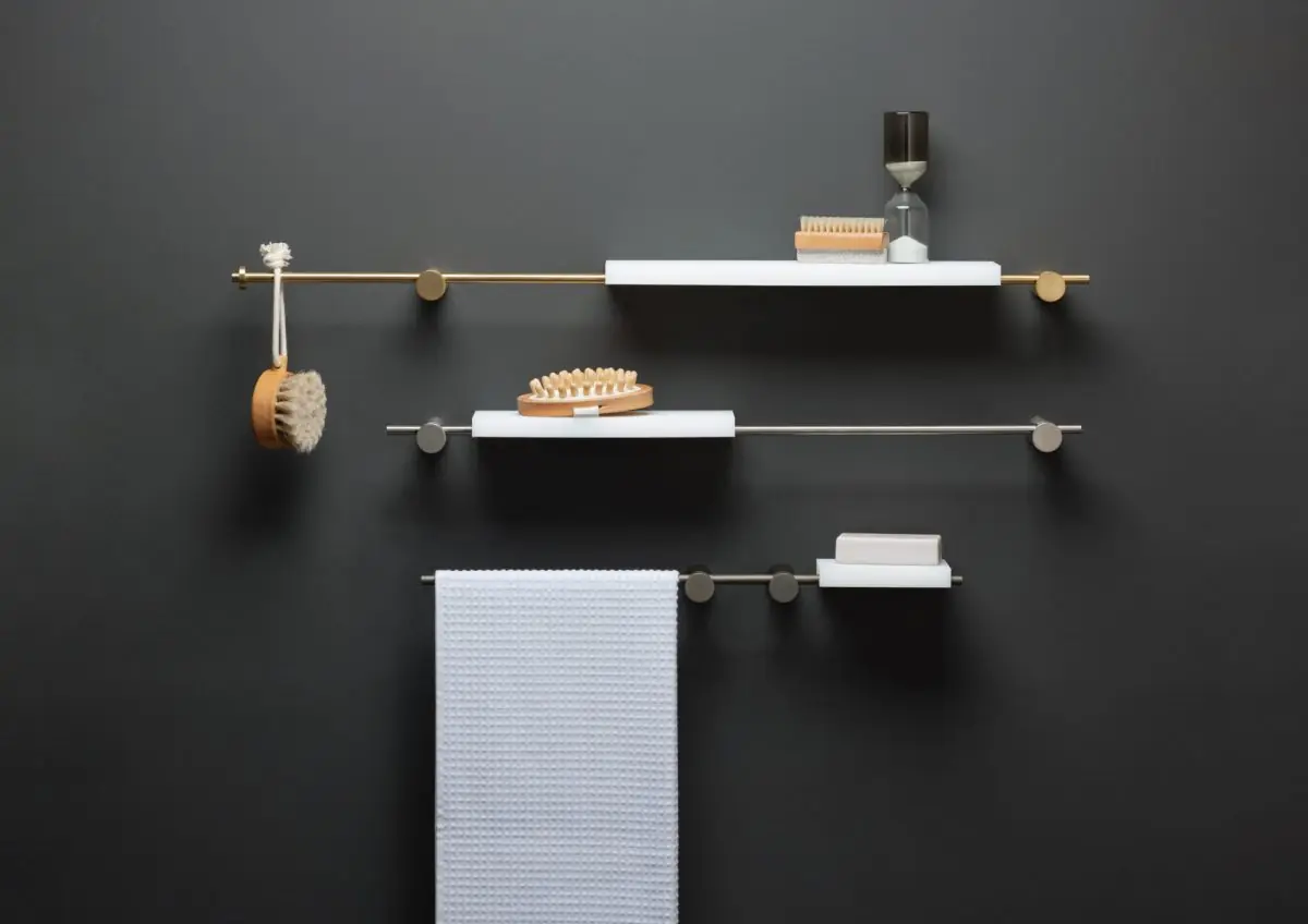 Tres composiciones de varillas metálicas en la pared con estantes blancos, una toalla, un cepillo y una pastilla de jabón