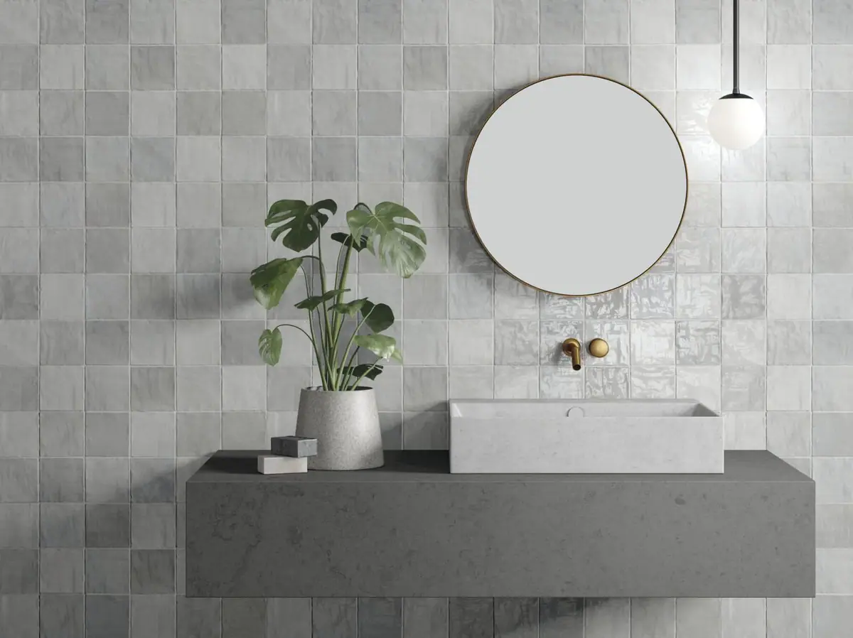 Baño con pared revestida de piezas cuadradas grises de esmalte irregular, espejo redondo y encimera gris con lavabo
