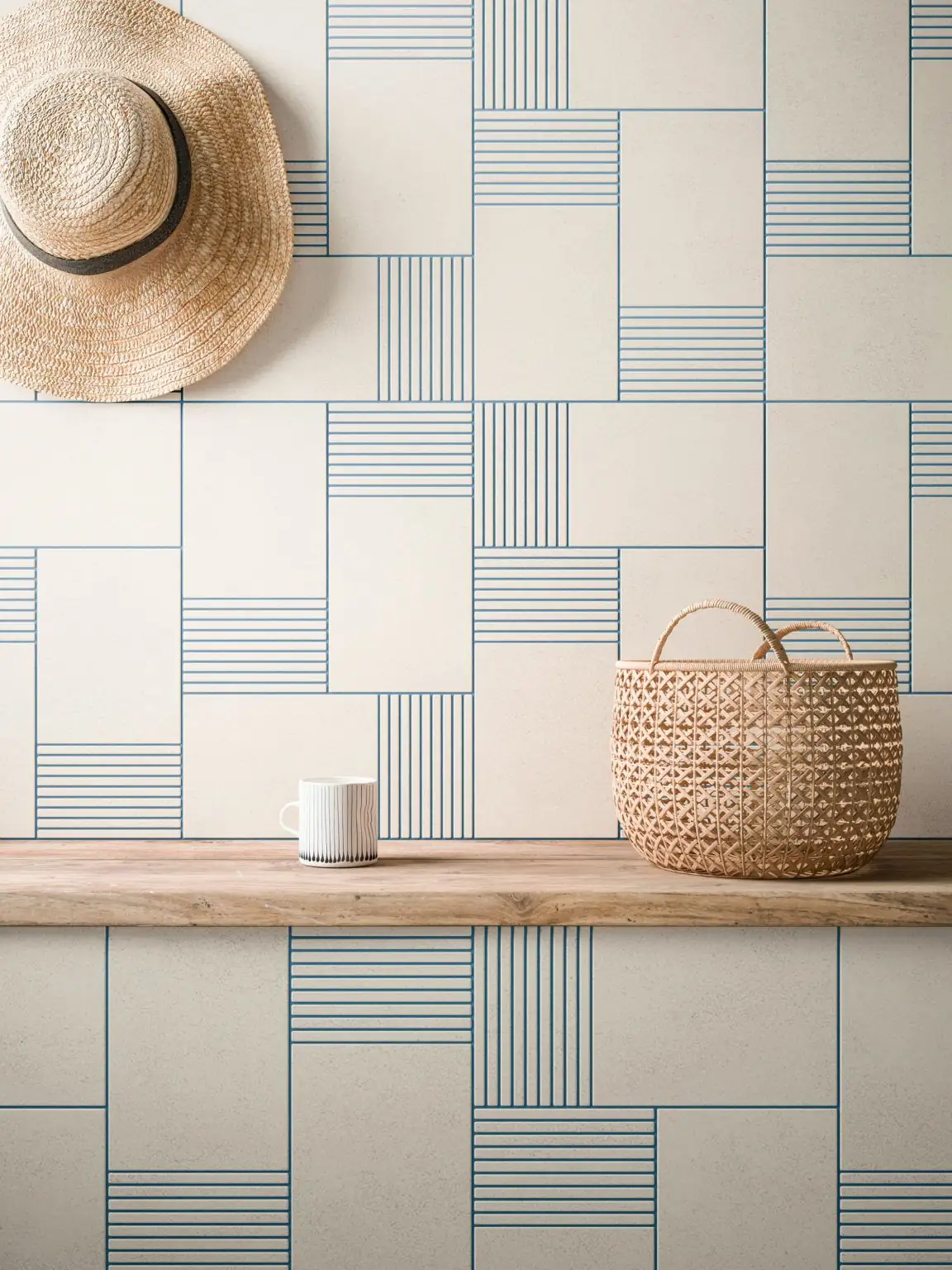 Pared de piezas blancas con decoraciones de líneas azules que alternan cuadros lisos y rayados, con un sombrero de paja y una cesta