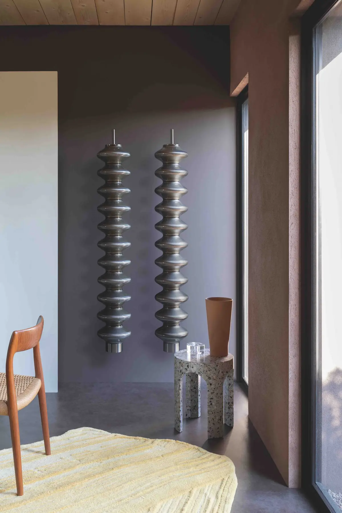 Dos radiadores Milano en gris oscuro montados en la pared de un salón, junto a una silla de madera
