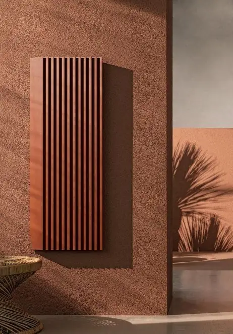 Radiador de aluminio plisado en color terracota sobre una pared del mismo tono
