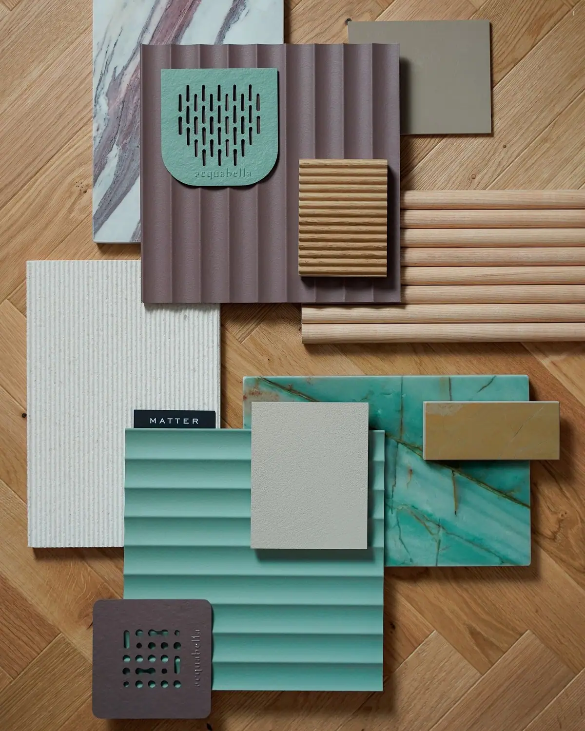 Composición de muestras de materiales sobre parquet con dos rejillas de plato de ducha de Acquabella y paneles con relieve en malva y verde agua