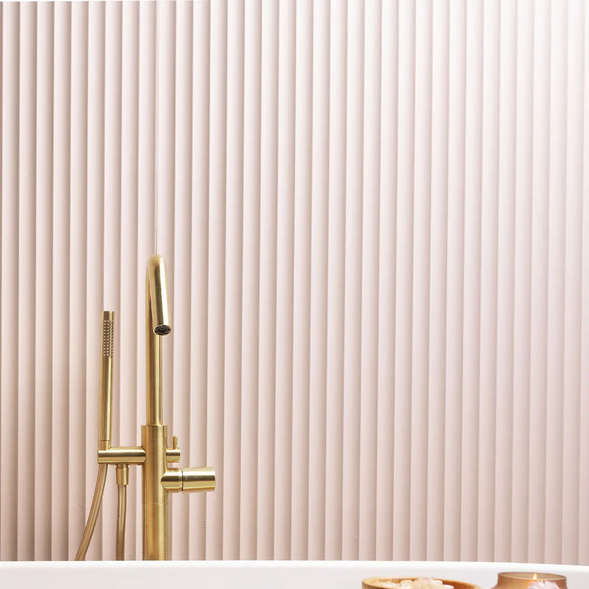 Pared revestida con panel de ondas verticales en tono rosa claro y grifería dorada de bañera