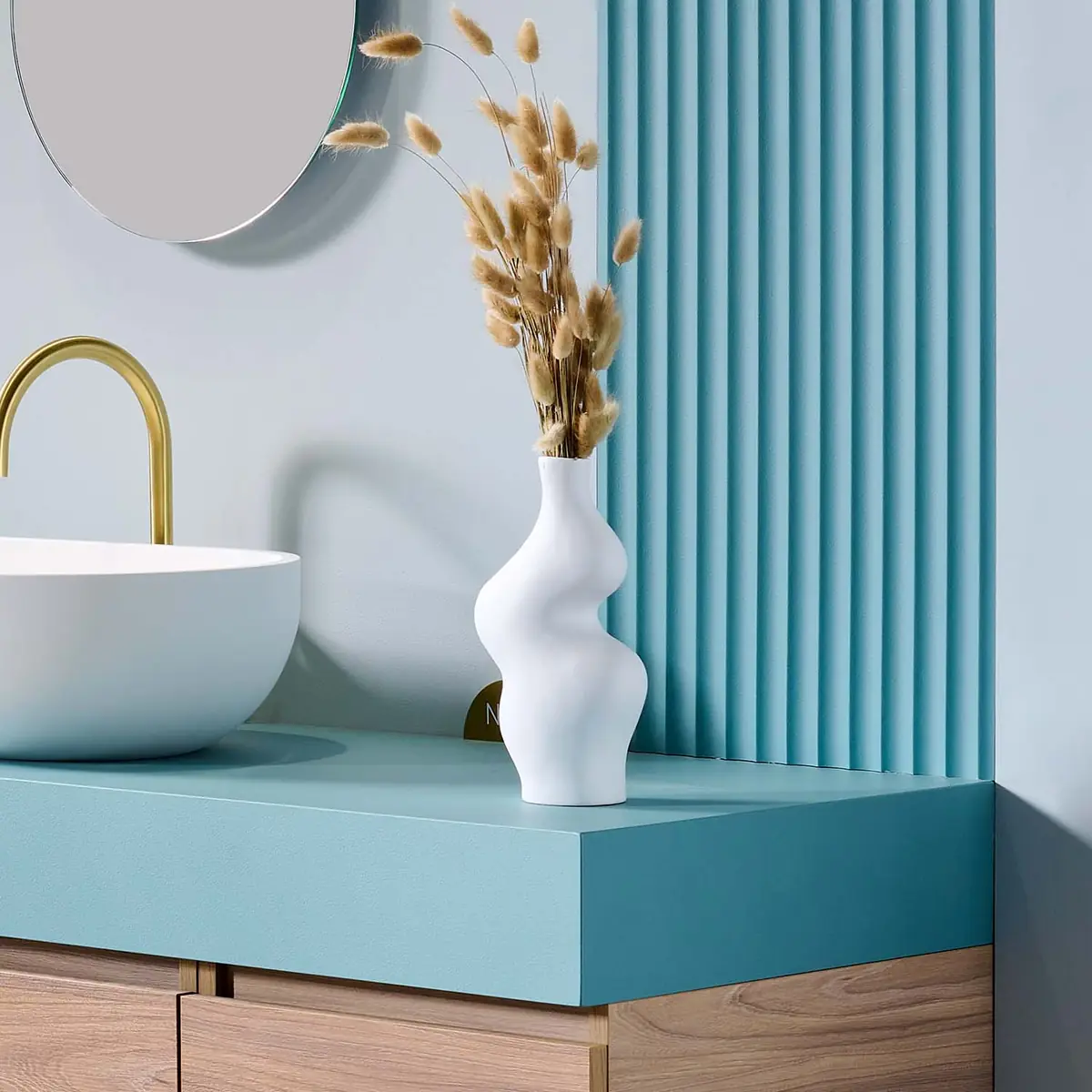 Panel de ondas verticales en azul tras una encimera del mismo color con lavabo blanco y grifería dorada