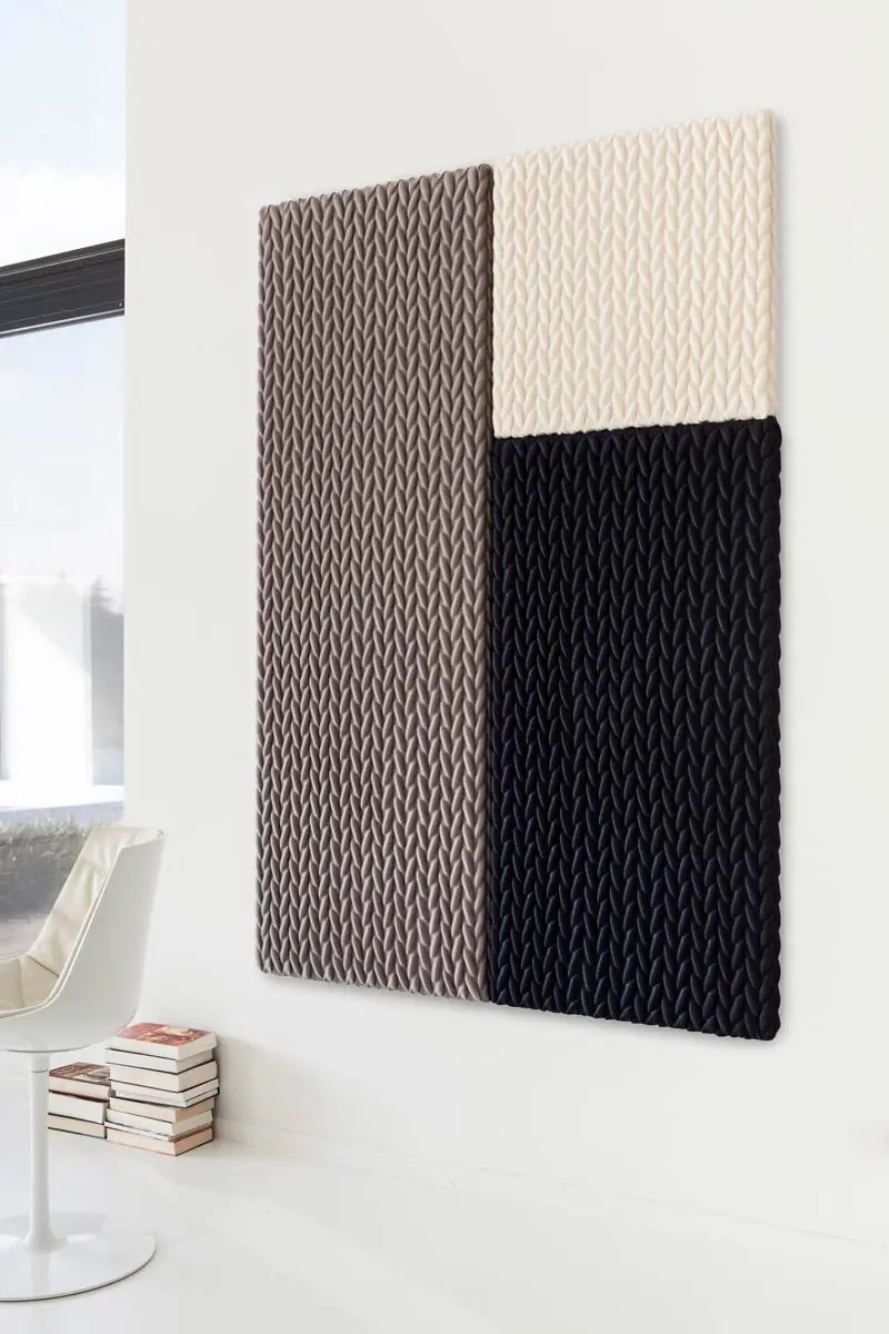 Composición mural de paneles acústicos textiles en relieve en gris pardo, crema y negro junto a una silla blanca