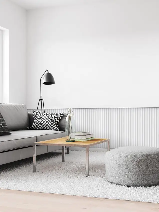 Salón blanco con sofá gris y la parte baja de la pared revestida con paneles de relieve vertical pintados en blanco.
