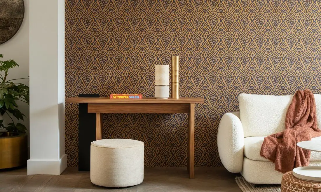 Pared revestida con un papel pintado de zigzag geométrico en ocre y azul, tras una consola de madera y un sofá blanco