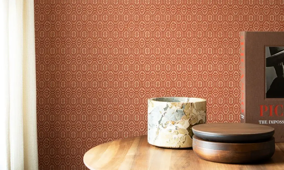 Pared con papel pintado de motivos geométricos cerrados en tonos teja y una mesa de madera con recipientes de mármol y madera