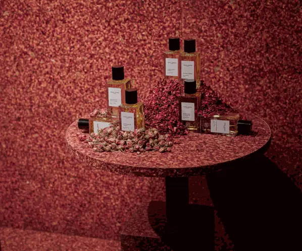 Pared y mesa revestidas con pétalos de rosa prensados, con frascos de perfume sobre la mesa