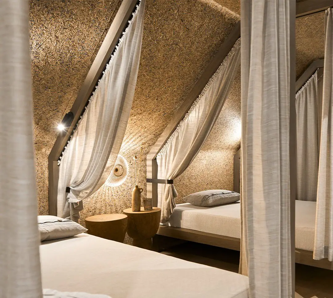 Dormitorio abuhardillado con camas con dosel y paredes y techo revestidos con una superficie de fibras vegetales
