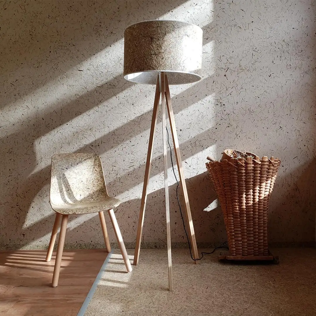 Silla, lámpara de pie y pared revestidas con superficies de heno, junto a una cesta de mimbre