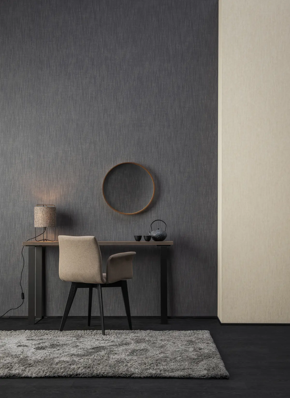 Zona de trabajo con escritorio, silla y espejo redondo ante una pared gris oscura, junto a un tabique en tono beige.