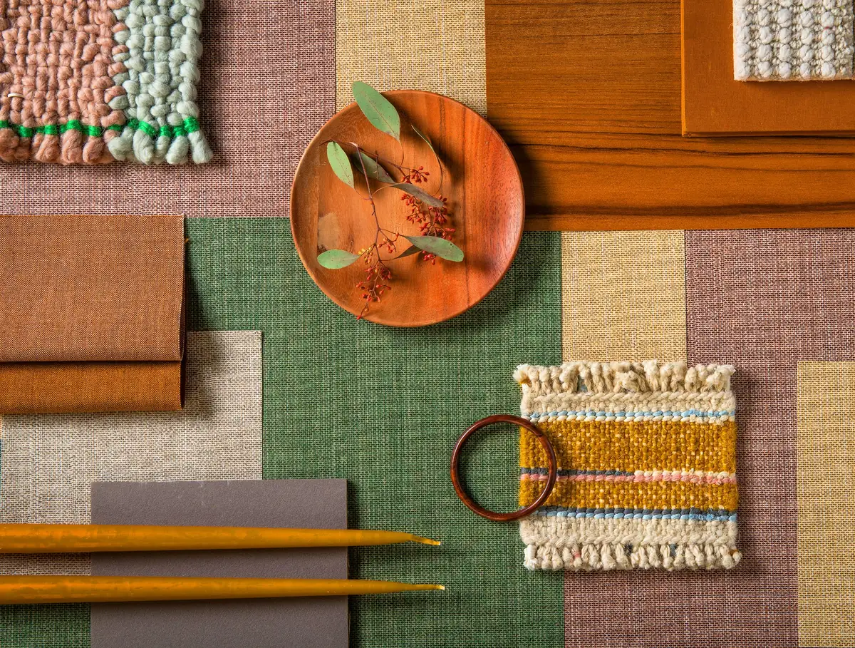 Composición de muestras de revestimiento en verde, rosa, beige y teja con un plato de madera, velas y un tapiz tejido.