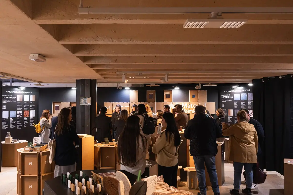 Visitantes recorren el espacio Materialidad Innovadora, con paneles negros a ambos lados y muestras sobre módulos de cartón