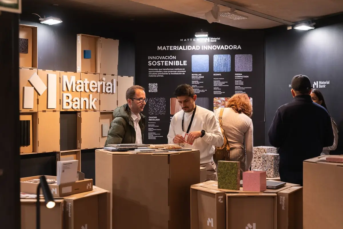 Dos visitantes conversan frente al panel Innovación sostenible y un muro de cajas con el logotipo de Material Bank