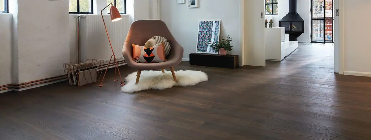 Salón con pavimento de tablas largas de madera oscura, butaca tapizada sobre una alfombra de pelo y chimenea al fondo