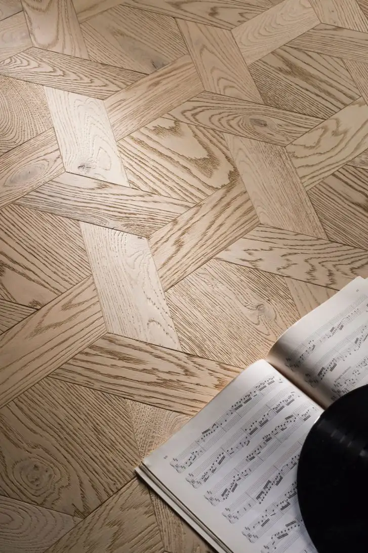 Pavimento de madera clara en formato Casablanca, con piezas geométricas entrelazadas, y una partitura y un disco de vinilo