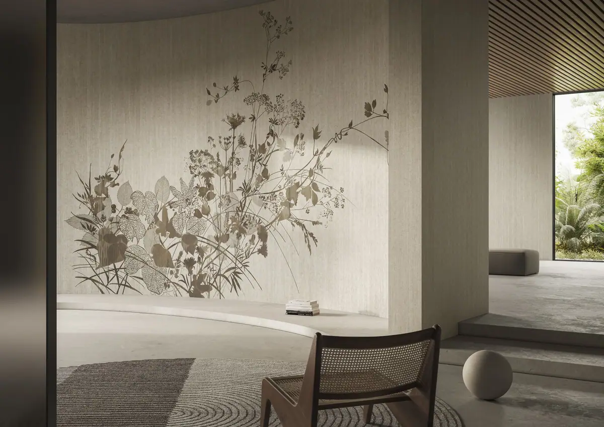 Pared curva revestida con un gran ramo de flores silvestres y hojas en tonos tierra, con una butaca de madera y rejilla en primer plano.