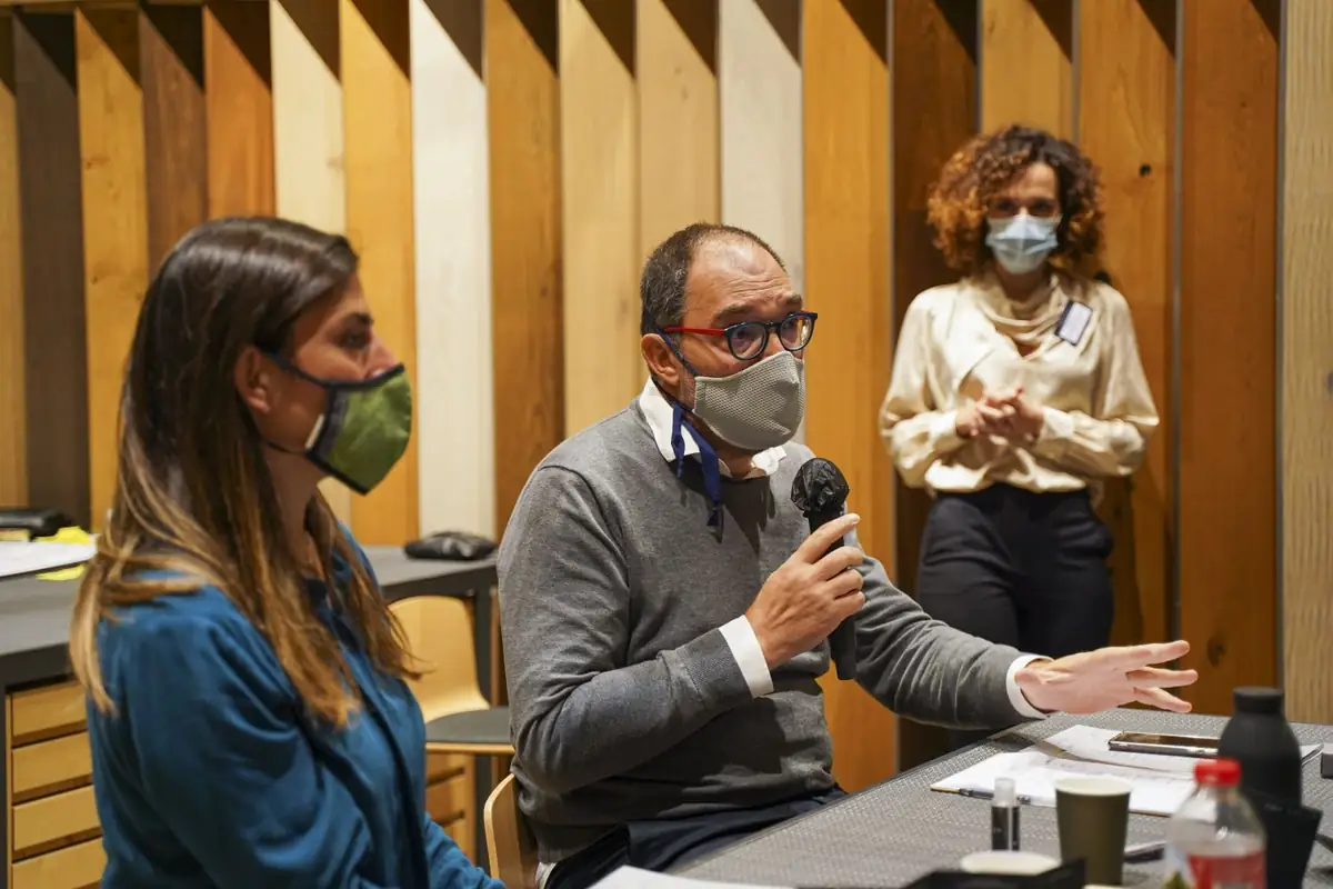 Un participante con mascarilla interviene con micrófono sentado a la mesa