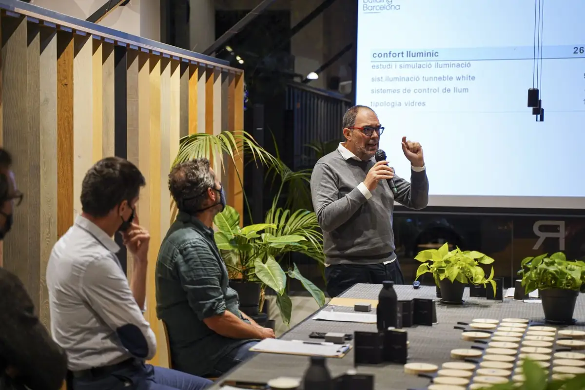 Un ponente gesticula con micrófono junto a una proyección dedicada al confort lumínico